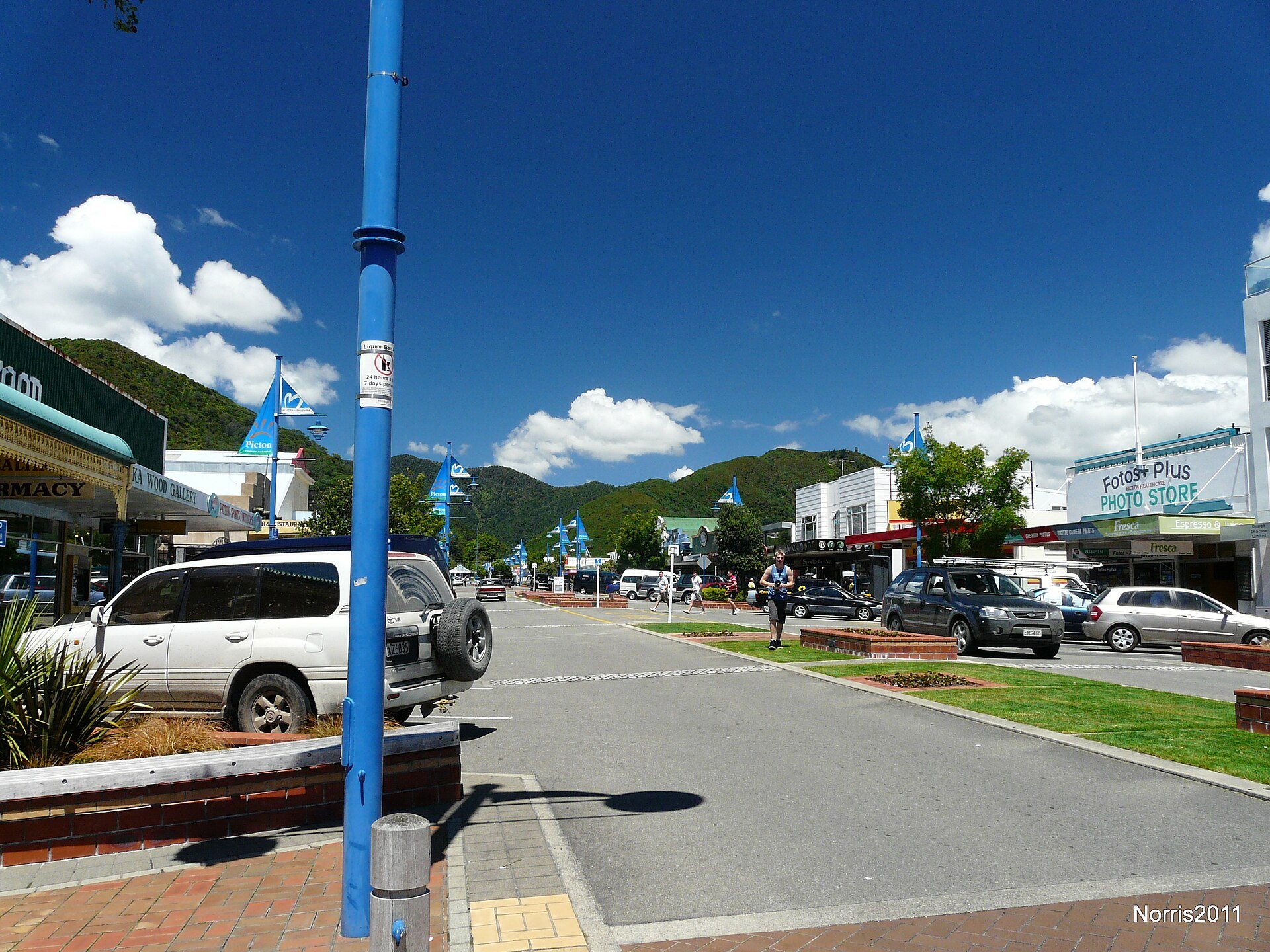 High Street looking south, shopfronts and a pharmacy along the footpath under a blue sky