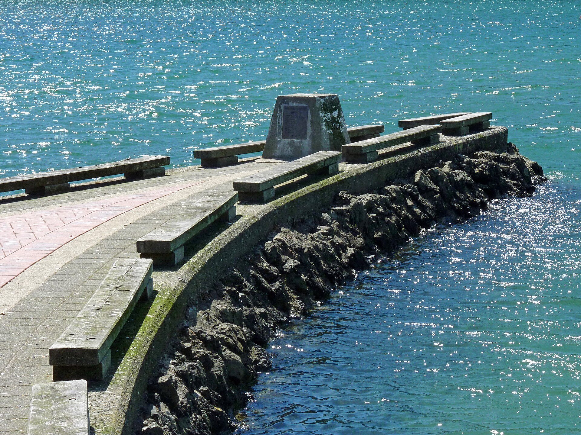 A curving stone seawall on Picton's waterfront reaching out over clear turquoise water