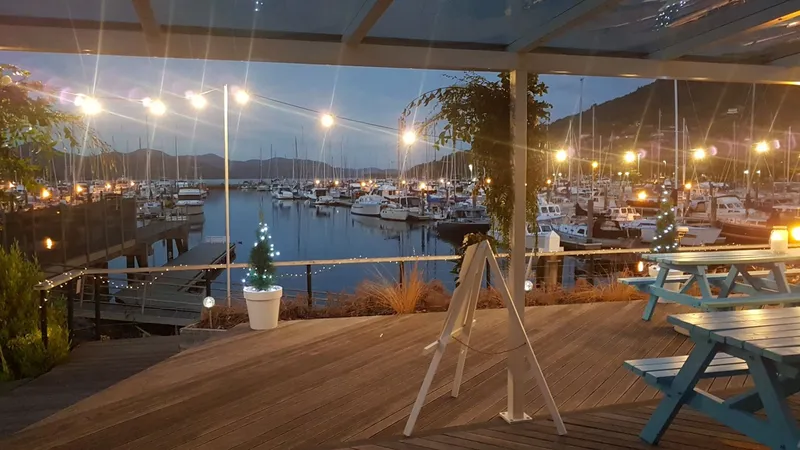 Outdoor deck seating overlooking boats in Waikawa Marina under evening lights.