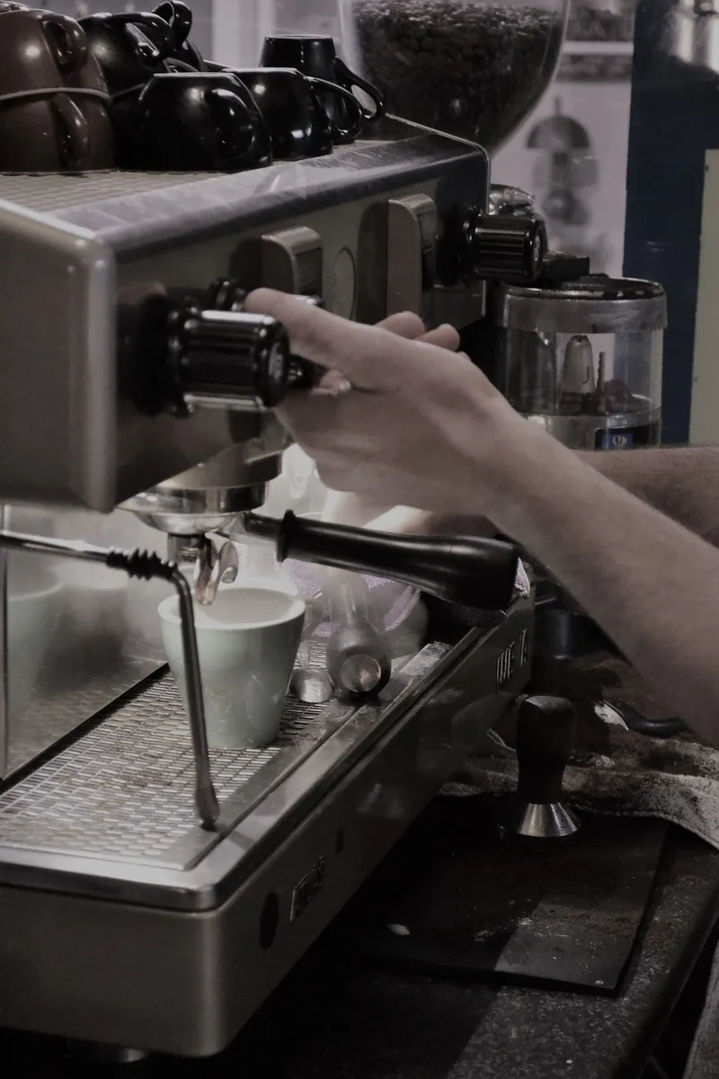 Barista operating the cafe's espresso machine, with cups and coffee grinder visible.