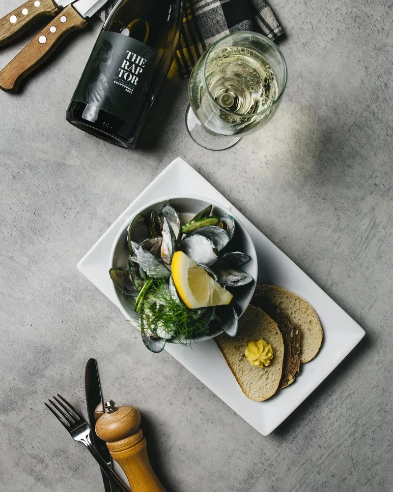 Bowl of green-lipped mussels with bread, lemon and a glass and bottle of Marlborough chardonnay.