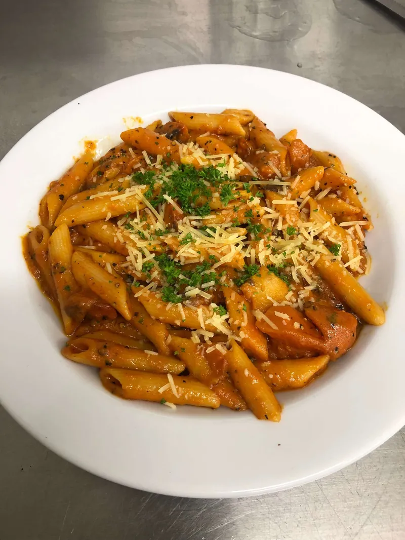 A bowl of penne pasta in tomato sauce, topped with grated cheese and parsley.