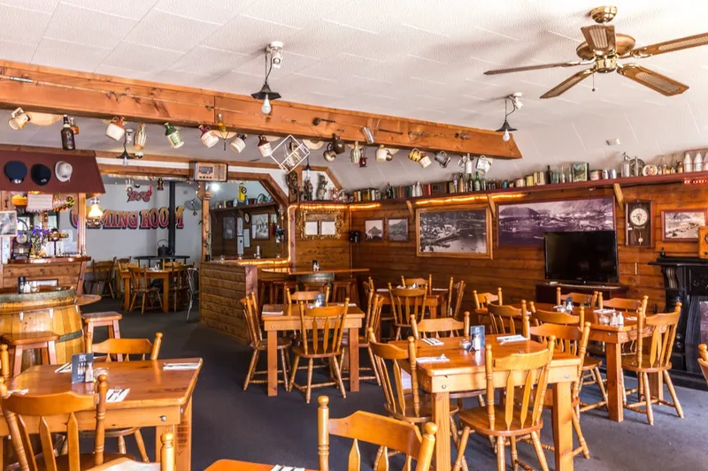 Wood-lined main dining room with set tables, barrel decor, historic photographs and bar area.