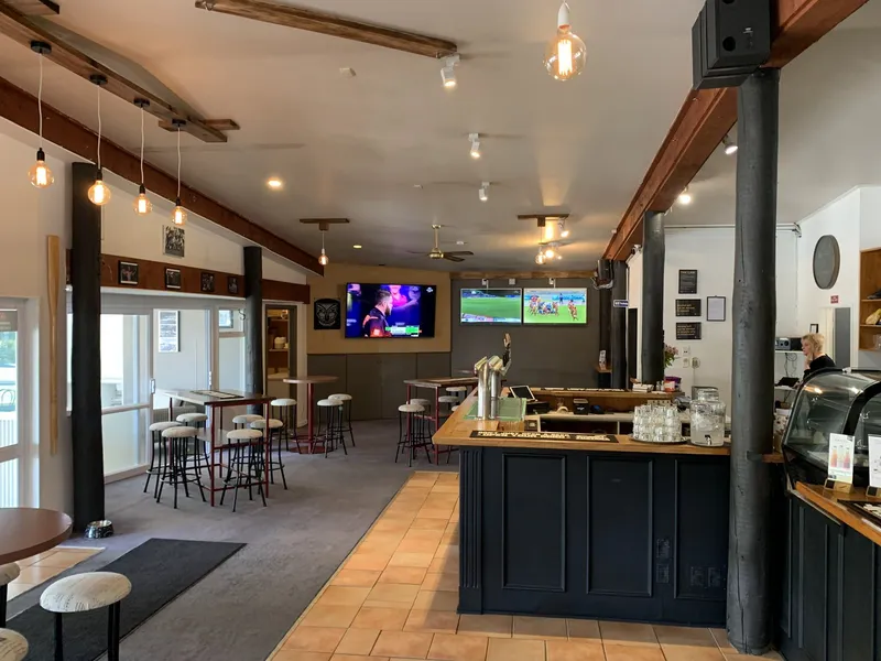 Wide view of the sports-bar interior with bar counter, taps, high tables, stools and wall-mounted televisions.