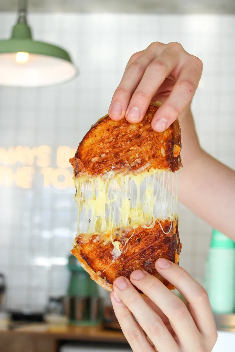 A toasted sandwich being pulled apart to show long strands of melted cheese inside.
