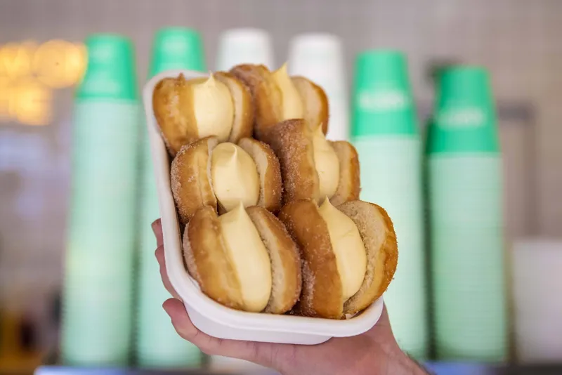 A tray piled with sugar-coated doughnuts filled generously with pale yellow cream.