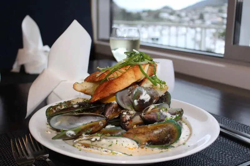 Green-lip mussels in a creamy sauce with toasted bread, photographed by a harbour-facing window.